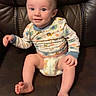 baby, infant, child, smiling, sitting, onesie, diaper, plush_toy, yellow_toy, leather_couch, indoor, cute, happy, face, person, young_child, furniture, toy, comfort, portrait