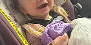 Ava is registered to the contest to win money with this photo: baby, infant, smiling, car_seat, seatbelt, blanket, purple_blanket, plush_toy, happy, close_up, portrait, hand, hair, cheek, clothing, fabric, warning_label, car_interior, sunlight, candid