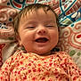 Ava is registered to the contest to win money with this photo: baby, infant, smile, laughing, onesie, floral_onesie, blanket, bedding, closeup, face, cheeks, hair, portrait, happy, newborn, adorable, lying_down, cozy, fabric_pattern, colorful