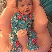 Ava is registered to the contest to win money with this photo: baby, infant, child, smiling, portrait, pink_inflatable_chair, onesie, floral_pattern, sitting, indoor, happy, hair, eyes, bottle_holder, diaper_bag, cozy, furniture, bedding, cute, footed_pajamas