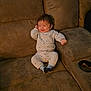 baby, infant, child, smiling, pajamas, socks, couch, sofa, upholstery, living_room, cup_holder, snack, face, hair, arm, seated, happy, portrait, cozy, furniture