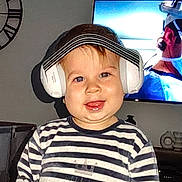 Pierre a rejoint le concours — aidez-le/la à gagner de superbes lots ! toddler, child, headphones, striped_shirt, smile, indoor, living_room, clock, television, face, cute, happy, person, baby, chubby_cheeks, short_hair, technology, casual_clothing, home, portrait