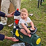 Pierre participe au concours pour gagner de l'argent avec cette photo : toddler, child, toy_train, outdoor, grass, plush_doll, adult_hands, steering_wheel, casual_clothing, playtime, happy, smiling, shorts, white_tshirt, blue_hat, red_pom_pom, striped_outfit, plastic_wheels, cardboard_box, green_toy