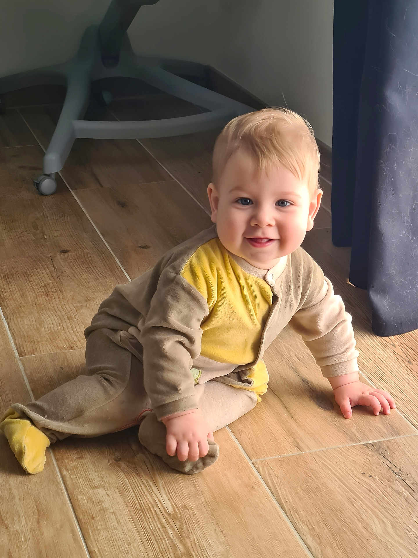 Pierre participe au concours pour gagner de l'argent avec cette photo : baby, child, smiling, floor, wooden_floor, onesie, clothing, indoor, person, curtain, furniture, hand, footwear, head, face, crawling, happy, blue_eyes, light, shadow