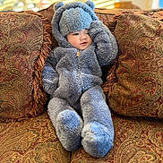 Zeke is registered to the contest to win money with this photo: baby, child, infant, teddy_bear_suit, fuzzy_onesie, hood, couch, sofa, decorative_pillow, paisley_pattern, plush, cozy, indoor, sunlight, portrait, smile, hand, legs, soft_texture, living_room