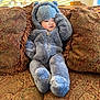 baby, child, infant, teddy_bear_suit, fuzzy_onesie, hood, couch, sofa, decorative_pillow, paisley_pattern, plush, cozy, indoor, sunlight, portrait, smile, hand, legs, soft_texture, living_room