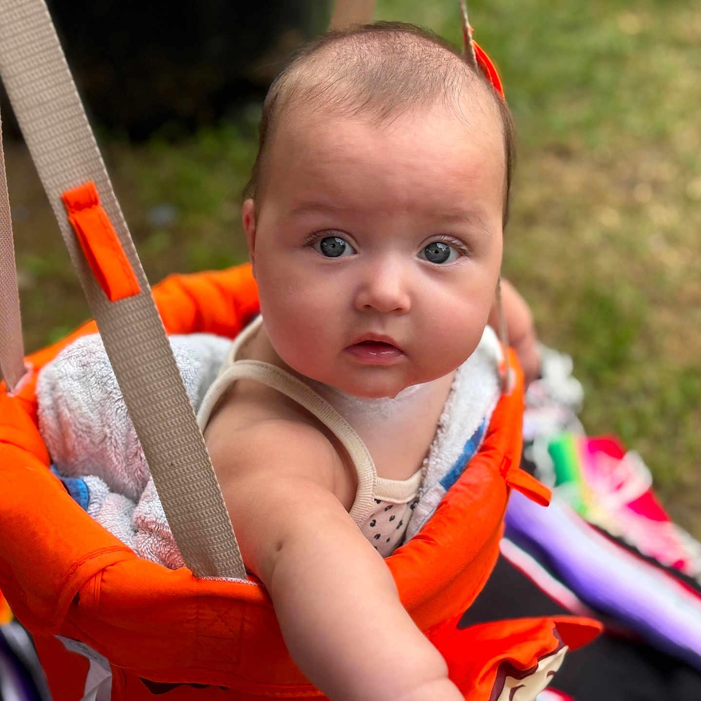 Sofia is registered to the contest to win money with this photo: baby, blanket, blue_eyes, child, closeup, curious, cute, expression, grass, infant, orange, outdoor, person, play, seat, skin, summer, swing, towel, young