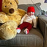 Jupiter is registered to the contest to win money with this photo: baby, teddy_bear, plush_toy, couch, sofa, red_hat, smile, infant, child, indoor, cozy, casual, festive_clothing, white_shirt, red_pants, socks, home, relaxing, cute, soft_toy