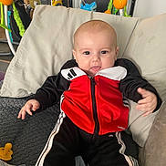 Kenny joined the competition — help win amazing prizes! baby, child, smiling, tongue_out, tracksuit, red_clothing, black_clothing, couch, pillow, toy, indoor, happy, person, infant, home, furniture, playful, casual_clothing, cute, relaxed