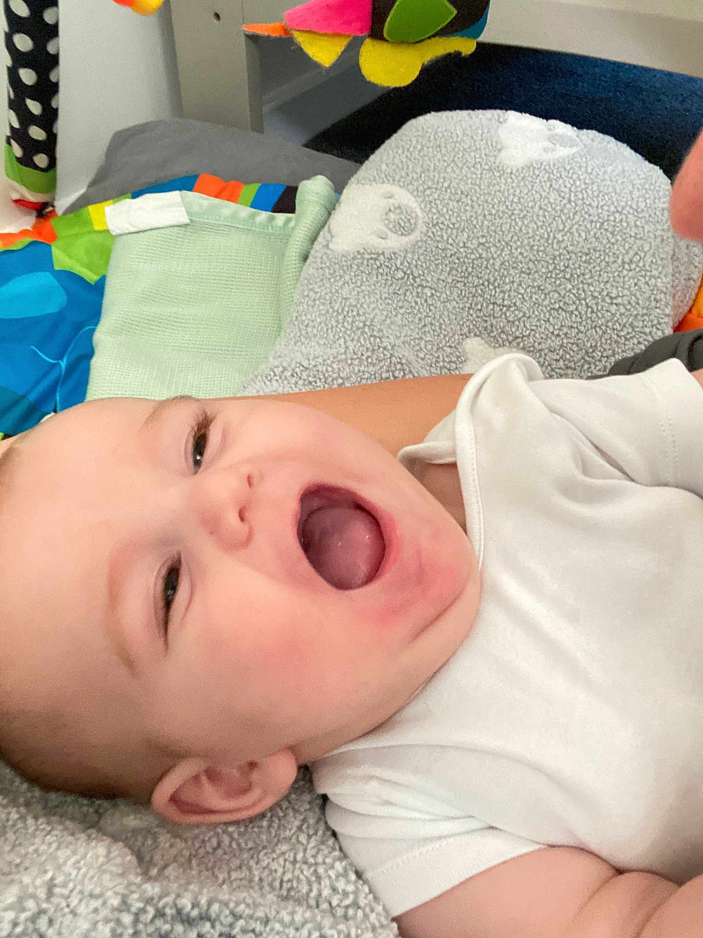 Kenny is registered to the contest to win money with this photo: baby, blanket, child, colorful, cute, face, happy, head, indoor, infant, laughing, mouth_open, person, play_area, skin, smiling, soft_texture, toy, white_clothing, young_child