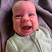 Silas is registered to the contest to win money with this photo: baby, smile, happy, infant, face, clothing, blanket, soft_texture, cute, lying_down, young_child, portrait, cozy, child, indoors, closeup, expression, baby_clothes, human, skin