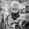 child, toddler, baby, portrait, face, serious, looking_at_camera, shopping_cart, supermarket, grocery_store, indoors, store_aisle, blanket, clothing, plaid, cart, black_and_white, sitting, retail, photograph
