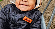 Shiloh joined the competition — help win amazing prizes! adorable, baby, black_jacket, carpet, child, close_up, face, handlebar, happy, hood, infant, jacket, outdoor, photography, portrait, sitting, smiling, sport_badge, stroller, winter_clothing