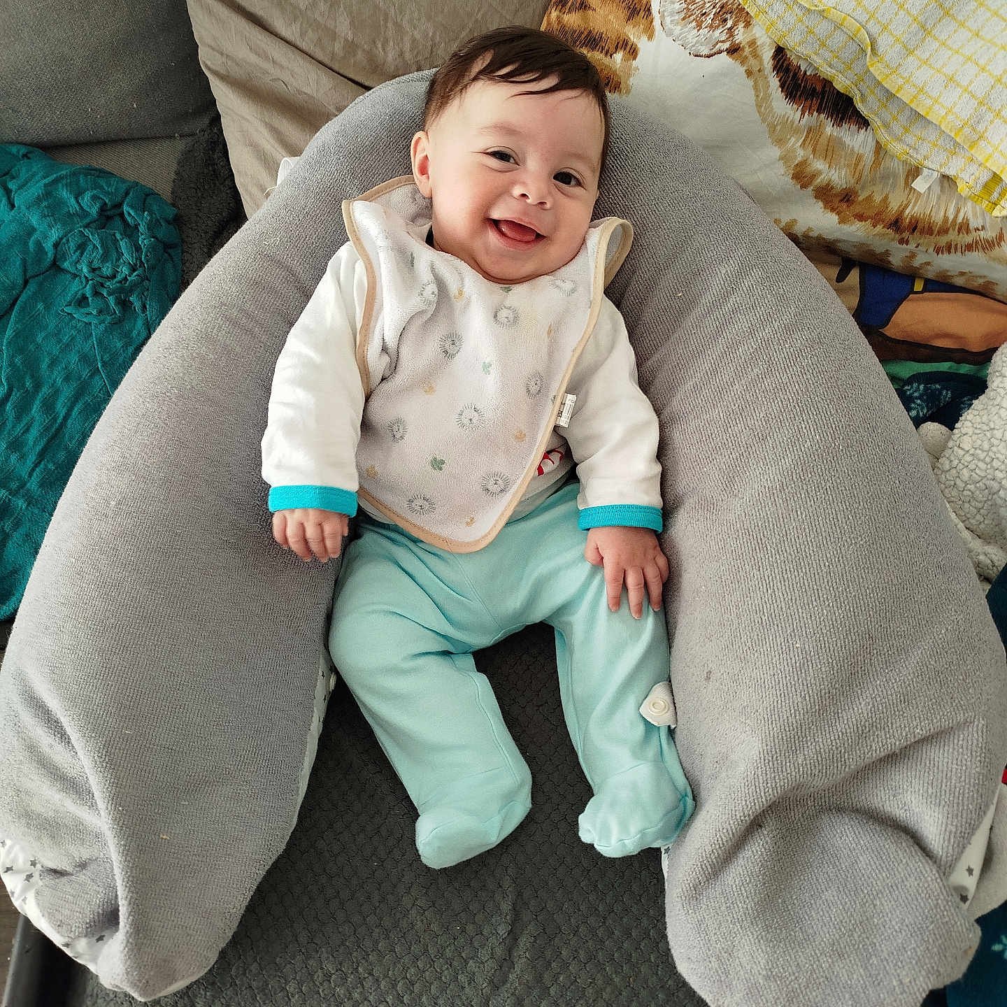 Tilyo a rejoint le concours — aidez-le/la à gagner de superbes lots ! baby, smiling, infant, bib, pillow, blanket, cushion, clothing, happy, person, indoor, comfort, relaxing, cute, child, portrait, seated, home, soft, cozy