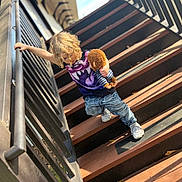 Jaxon is registered to the contest to win money with this photo: blue_jeans, careful, casual_clothing, child, climbing, curly_hair, daylight, holding, outdoor, person, playful, plush_monkey, railing, shadow, sneakers, stairs, sunlight, toy, wood, young
