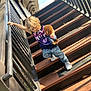 blue_jeans, careful, casual_clothing, child, climbing, curly_hair, daylight, holding, outdoor, person, playful, plush_monkey, railing, shadow, sneakers, stairs, sunlight, toy, wood, young