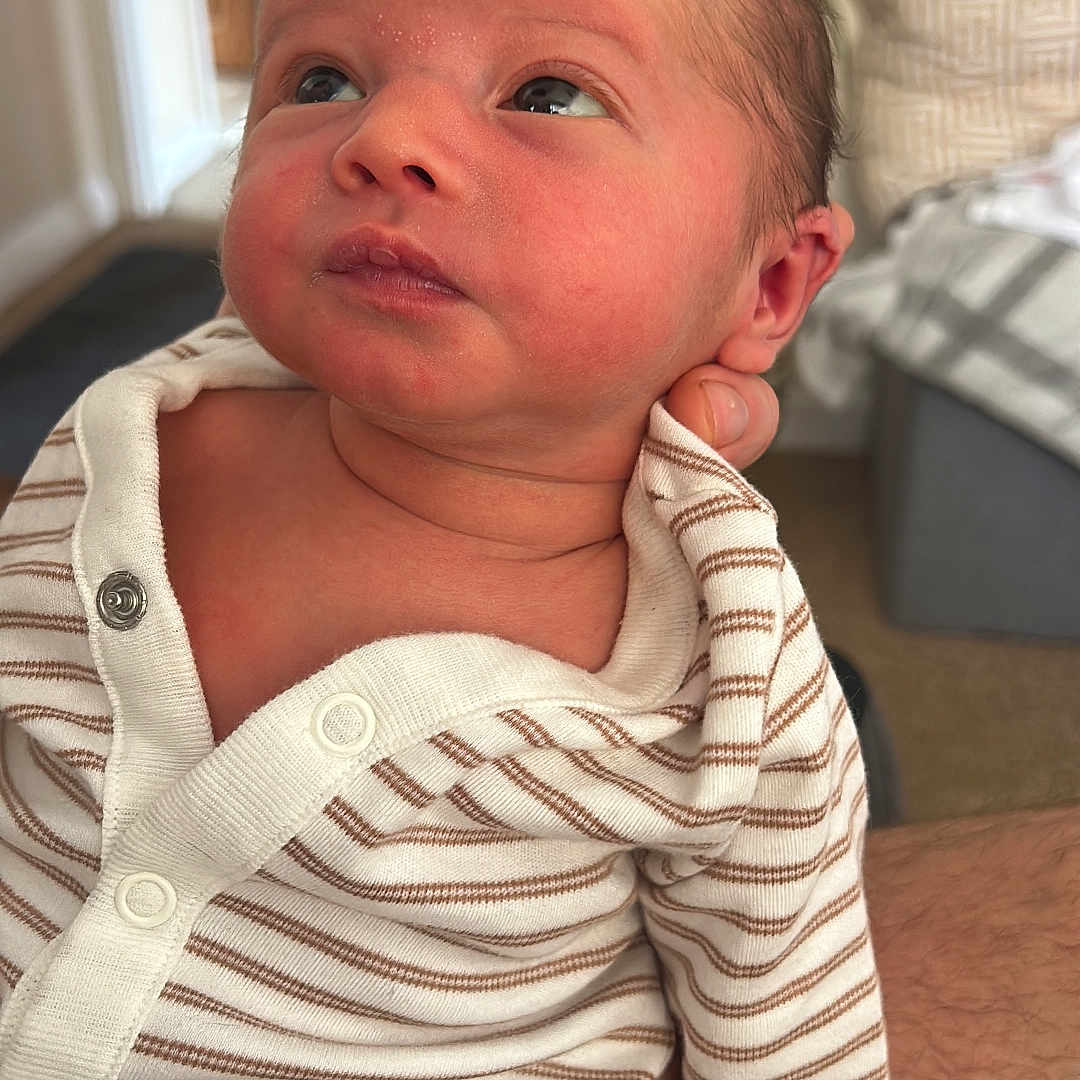 Aoife joined the competition — help win amazing prizes! adult_arm, baby, blanket, closeup, couch, cozy, curious, face, gaze, head, human_skin, indoor, infant, newborn, onesie, person, plant, portrait, soft_light, striped_clothing