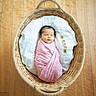 newborn, baby, basket, blanket, pink, wooden_floor, wooden_blocks, letters, sleeping, cute, infant, swaddled, heart_pattern, white_cushion, indoors, peaceful, portrait, cozy, resting, child