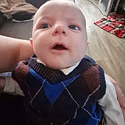 Eliot a rejoint le concours — aidez-le/la à gagner de superbes lots ! baby, child, person, face, sweater, vest, argyle, indoor, living_room, blanket, chair, floor, toy, hand, wide_eyes, curious, seated, clothing, home, person_holding_child