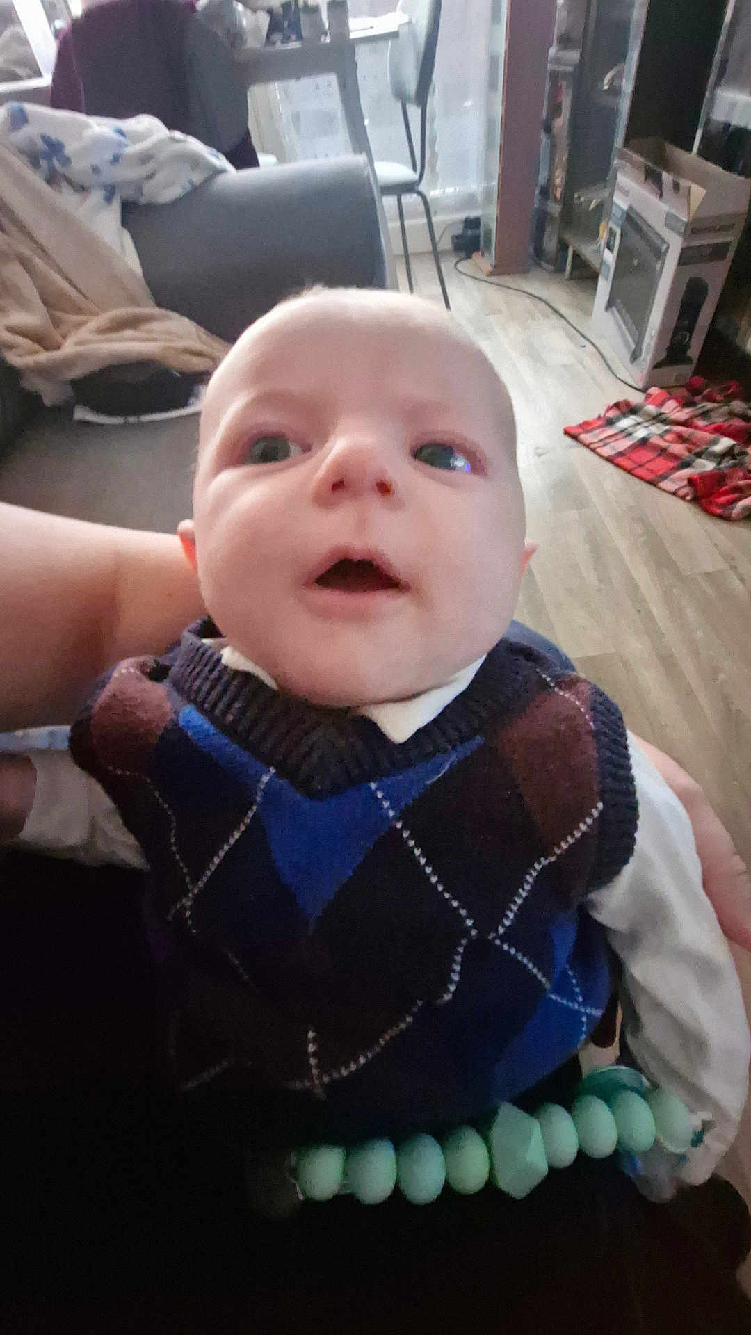 Eliot a rejoint le concours — aidez-le/la à gagner de superbes lots ! baby, child, person, face, sweater, vest, argyle, indoor, living_room, blanket, chair, floor, toy, hand, wide_eyes, curious, seated, clothing, home, person_holding_child