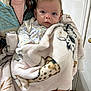 baby, infant, person, blanket, plush_blanket, onesie, face, eyes, gaze, holding, adult_arm, cozy, indoors, door, light_switch, soft_texture, portrait, clothing, pattern, skin