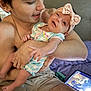 baby, infant, adult, holding, smile, headband, bow, onesie, striped_clothing, arm, bare_chest, tablet, screen, bed, blanket, closeup, portrait, happy, indoor, family_moment