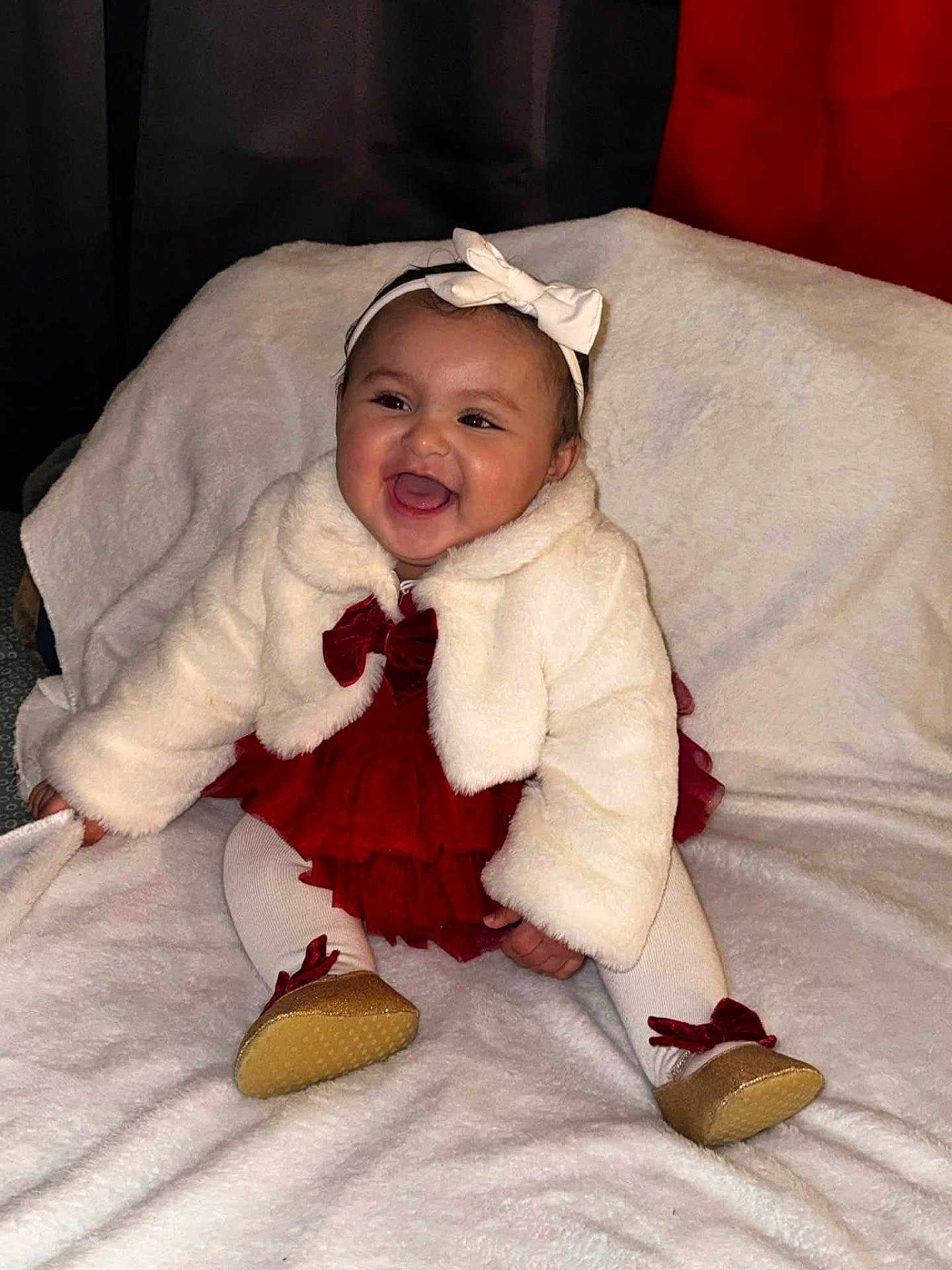 Lillian is registered to the contest to win money with this photo: baby, child, smile, white_jacket, red_dress, headband, bow, tights, golden_shoes, blanket, happy, sitting, cute, indoors, portrait, infant, fashion, warm_clothing, cheerful, adorable