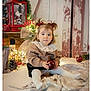 Leiya participe au concours pour gagner de l'argent avec cette photo : toddler, child, girl, pigtails, ribbon, christmas, holiday_decor, ornament, lantern, fairy_lights, blanket, wooden_wall, nutcracker, pinecone, sitting, portrait, cute, indoor, cozy, props