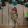 Naveen joined the competition — help win amazing prizes! child, toddler, woman, mother, portrait, birthday, balloons, balloon_arch, party, celebration, smiling, sitting, holding, indoors, decorations, green, black, silver, tile_floor, family