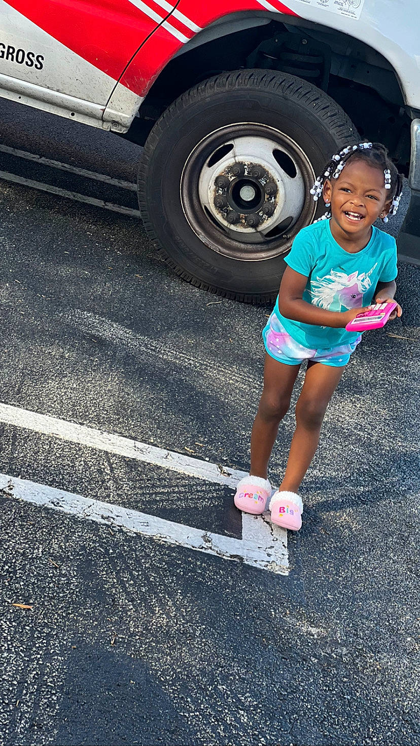 Teyana is registered to the contest to win money with this photo: asphalt, automotive_design, automotive_lighting, automotive_tire, bumper, car, face, fender, hat, hubcap, infrastructure, leg, motor_vehicle, person, road_surface, shorts, smile, tire, vehicle, vehicle_door