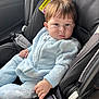 baby, child, car_seat, seatbelt, blue_onesie, infant, hand, face, hair, car_interior, safety, child_safety_seat, clothing, young_child, portrait, cute, serious_expression, person, indoors, seat