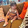 Alana is registered to the contest to win money with this photo: toddler, child, smiling, couch, pillow, indoors, public_space, clothing, patterned_outfit, pink_shoes, hair_bows, happy, sitting, person, furniture, casual, background_people, window, decor, earrings