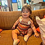 Alana is registered to the contest to win money with this photo: toddler, child, couch, smile, indoors, colorful_clothing, patterned_outfit, happy, sitting, cushion, brown_couch, playful, young_child, cute, furniture, portrait, casual, home, person, interior