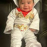 Ezra is registered to the contest to win money with this photo: baby, child, smile, white_clothing, red_socks, elvis_costume, cute, portrait, sitting, leather_chair, hair, infant, happy, young_child, indoors, fashion, costume, person, candid, funny