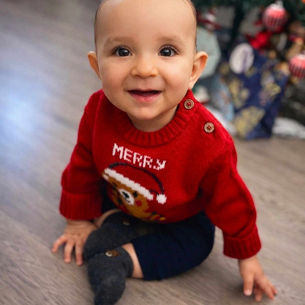 Mylann participe au concours pour gagner de l'argent avec cette photo : baby, child, smiling, red_sweater, christmas, holiday, floor, present, gift_wrap, tree, decorations, indoors, cute, toddler, happy, seasonal, festive, portrait, clothing, sock