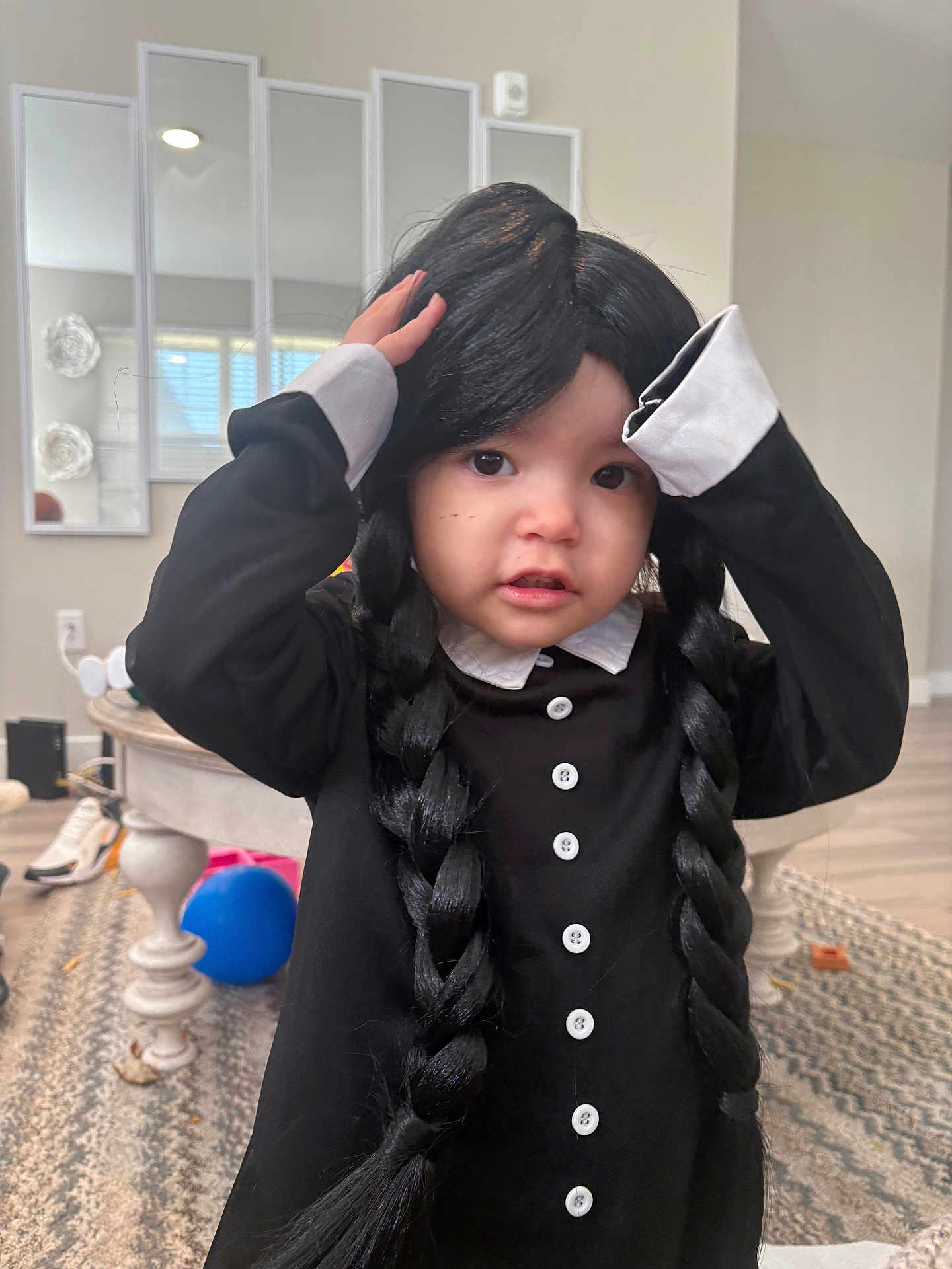 Lady is registered to the contest to win money with this photo: child, toddler, wig, braids, black_clothing, buttons, white_collar, indoor, living_room, carpet, table, ball, shoes, mirror, window, person, cute, portrait, hands_on_head, floor