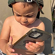 Zaïm a rejoint le concours — aidez-le/la à gagner de superbes lots ! bare_chest, camo_cap, child, curious, fingers, focused, hand, hat, lounge_chair, outdoor, phone, portrait, relaxation, skin, smartphone, summer, sunlight, technology, toddler, towel