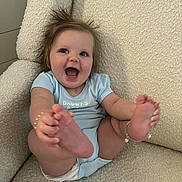 Boston is registered to the contest to win money with this photo: baby, infant, smiling, happy, blue_onesie, barefoot, armchair, beige, textured_fabric, indoor, cute, child, person, playful, hair, skin, foot, hand, sitting, joy