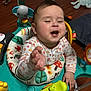 baby, child, activity_center, toy, smiling, playful, indoor, colorful, clothing, face, hand, floor, happy, infant, person, seat, expression, playtime, cute, toddler