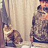 Leo is registered to the contest to win money with this photo: bathroom, mirror, selfie, young_man, hoodie, camo_clothing, cat, fluffy_cat, tabby_cat, sink, faucet, shower_curtain, towel, countertop, toothbrush, phone, reflection, indoor, portrait, casual