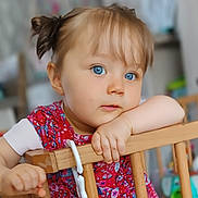 Maéliah participe au concours pour gagner de l'argent avec cette photo : baby, blue_eyes, child, clothing, curious, cute, expression, face, furniture, hand, home, indoors, person, pigtails, portrait, red_dress, toddler, toy, wooden_gate, young_child