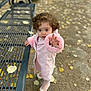 toddler, child, pink_coat, curly_hair, outdoor, bench, autumn_leaves, ground, park, walking, curious, reaching_hand, footwear, path, nature, fall, young_child, person, daylight, clothing