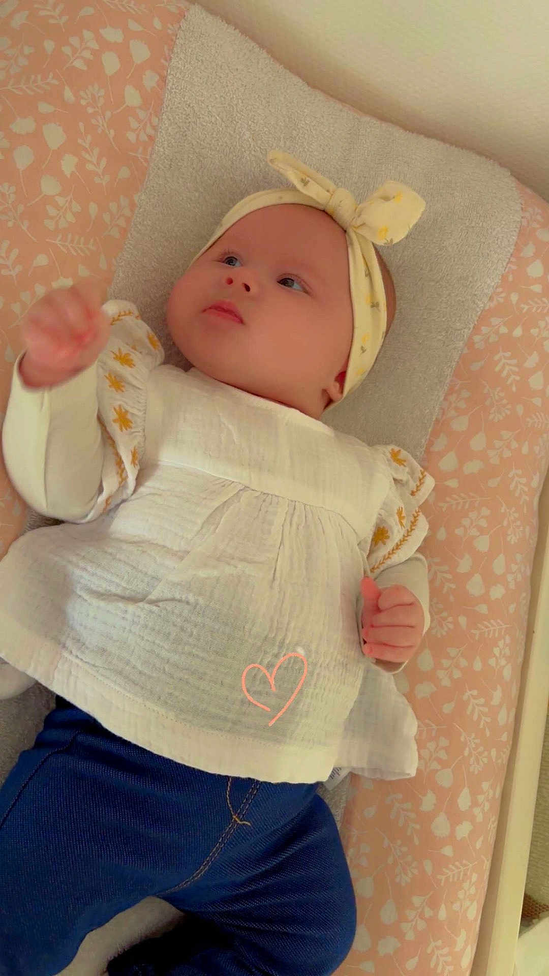 Léonie participe au concours pour gagner de l'argent avec cette photo : baby, child, infant, headband, dress, blue_pants, lying_down, patterned_changing_pad, pink, white, yellow, curious, soft_lighting, indoor, cute, adorable, clothing, person, young_child, portrait