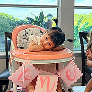 Selena joined the competition — help win amazing prizes! baby, child, high_chair, sitting, smiling, portrait, birthday, decorations, pink, indoors, window, sunlight, plants, table, family, infant, dark_hair, ponytails, celebration, home
