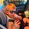 Wesley is registered to the contest to win money with this photo: child, toddler, boy, sunglasses, car, car_seat, seatbelt, vehicle, travel, road_trip, drinking_cup, straw, sunlight, portrait, sitting, indoors, warm_lighting, smiling, short_hair, family