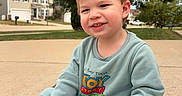 Wesley is registered to the contest to win money with this photo: child, toddler, boy, smiling, portrait, outdoor, driveway, suburb, house, trees, casual_clothing, sweatshirt, toy_story, pixar, cartoon, seated, sneakers, blond_hair, daylight, happy
