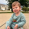 child, toddler, boy, smiling, portrait, outdoor, driveway, suburb, house, trees, casual_clothing, sweatshirt, toy_story, pixar, cartoon, seated, sneakers, blond_hair, daylight, happy