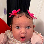 Azariah is registered to the contest to win money with this photo: baby, infant, face, expression, pink_bow, mittens, floral_outfit, cute, child, indoors, person, portrait, wide_eyes, surprised, head, hair, hand, clothing, baby_girl, closeup