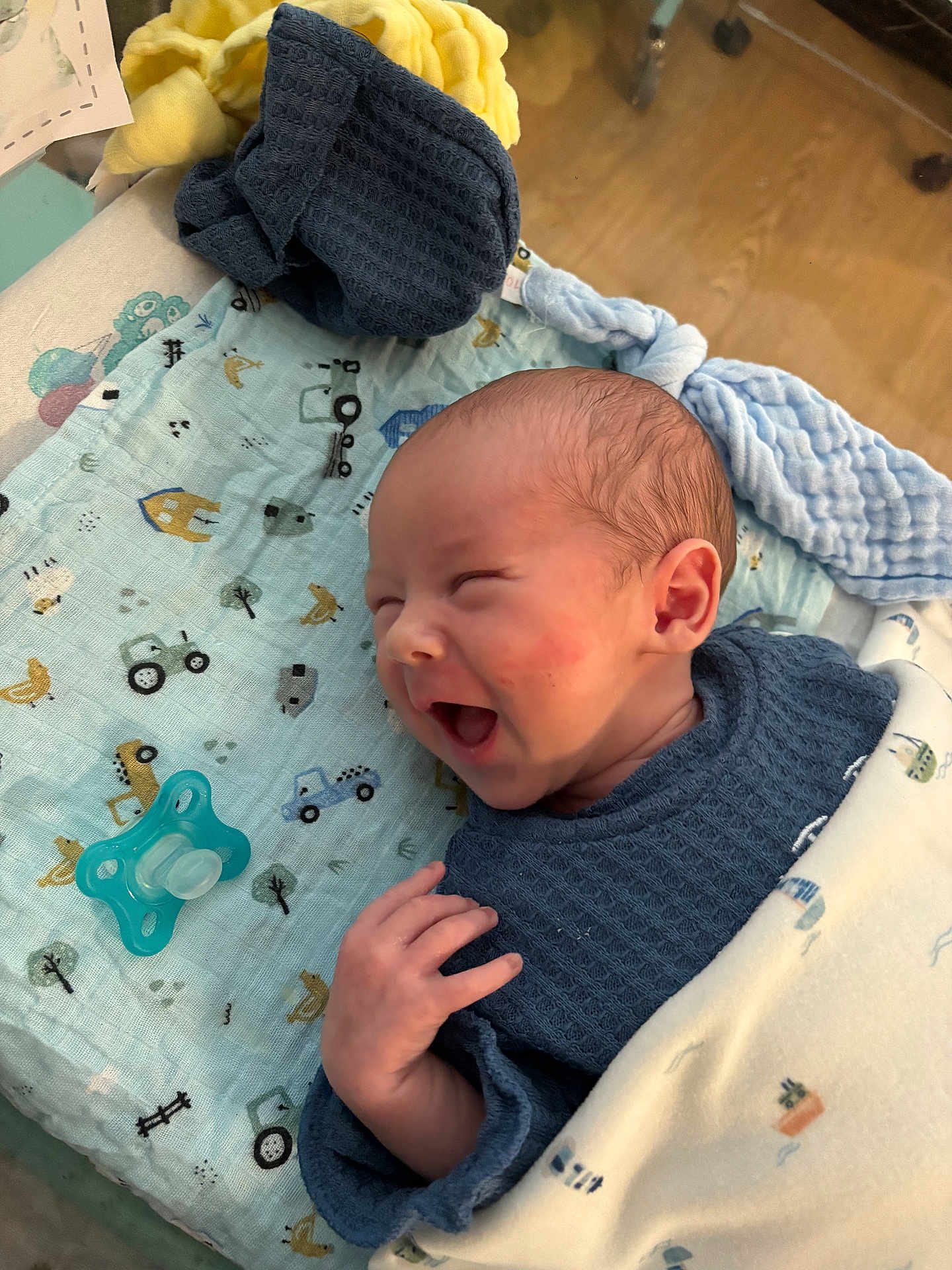 Mason joined the competition — help win amazing prizes! baby, newborn, infant, smiling, yawning, blue_clothing, blanket, pacifier, patterned_cloth, hand, face, head, skin, indoors, floor, wooden_floor, sleepwear, cute, cozy, happy
