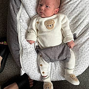 Mason is registered to the contest to win money with this photo: baby, infant, knitwear, teddy_bear, baby_seat, blanket, carpet, footwear, slide_sandals, soft_texture, resting, cozy, indoors, cute, child, newborn, white_clothing, pattern, comfort, home